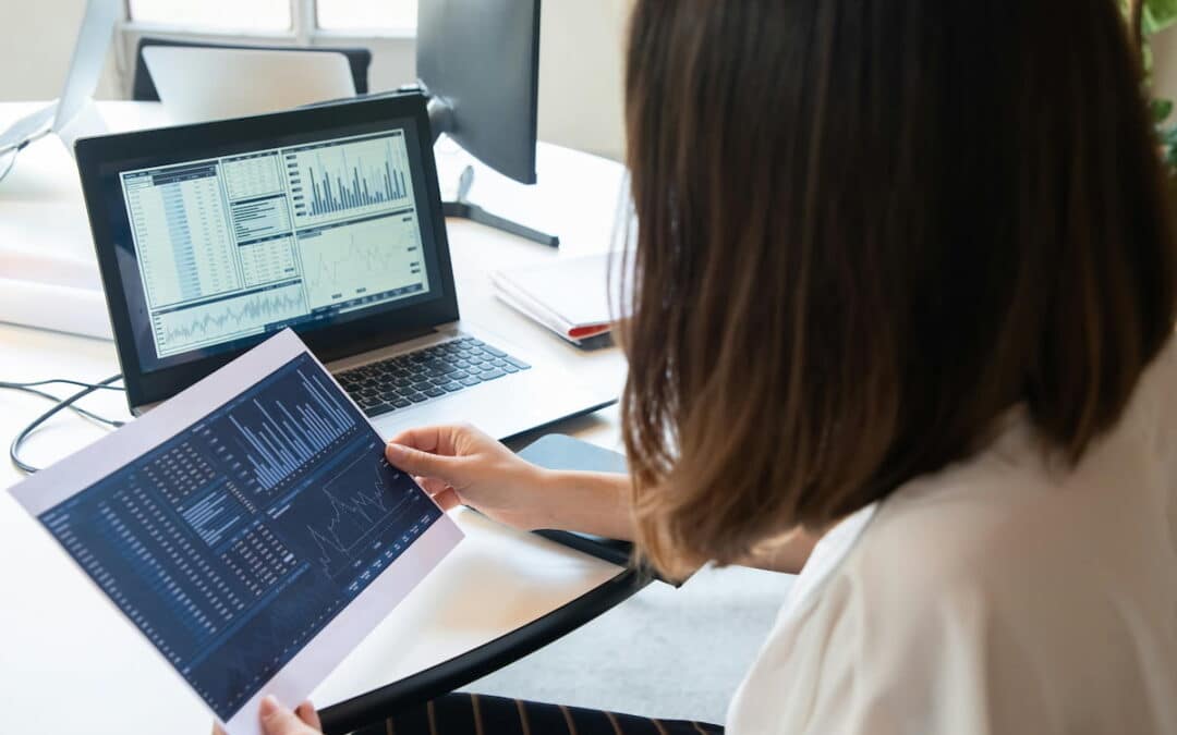 Billing analyst comparing revenue cycle reports across two screens at a desk