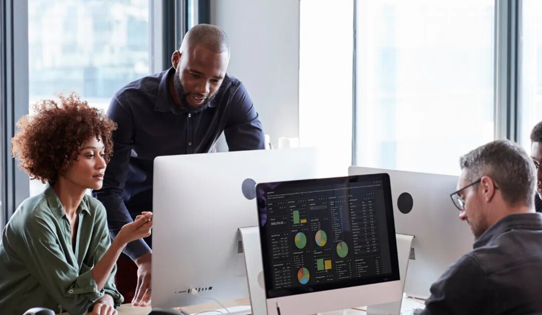 Team of healthcare revenue cycle professionals collaborating around a computer showing a data dashboard
