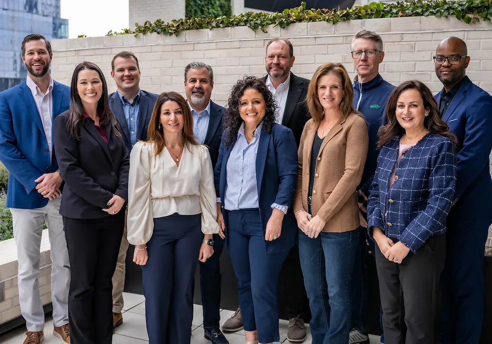 The AcuServe team of diverse professionals in business attire poses together outdoors in front of a brick wall.