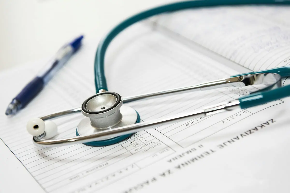 A teal stethoscope rests on top of a medical document next to a blue pen on a surface
