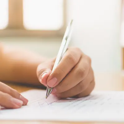 A close-up of a person's hand holding a pen and carefully writing on a paper document