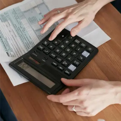 A person using a black electronic calculator while reviewing financial tax documents on a wooden table