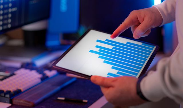 Hands pointing to horizontal data charts on a tablet screen at an office workstation.