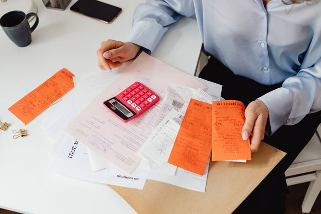 An overhead shot of a specialist organizing billing paperwork, receipts, and a calculator at a desk.
