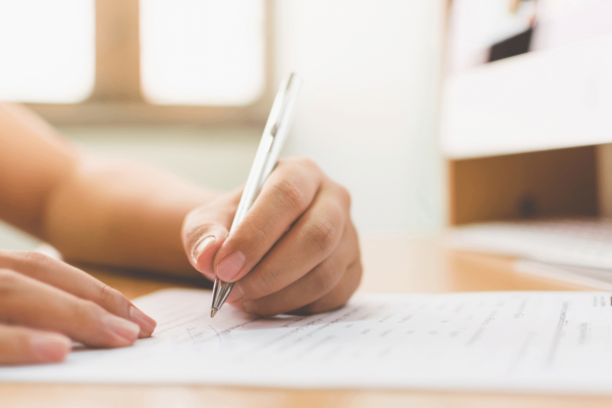 A teal stethoscope rests on top of a medical document next to a blue pen on a surface