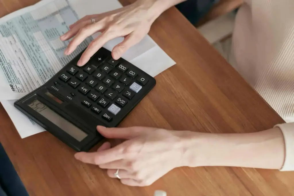 Overhead view of hands using a calculator next to a printed tax form on a wooden desk