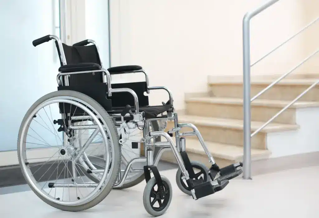 An empty manual wheelchair parked in a hallway near a staircase with a metal handrail